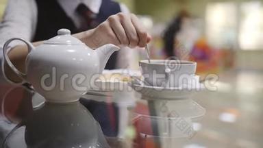十几岁的女孩在学校食堂里的一杯茶里搅拌糖一茶匙。 一个女孩在杯中搅拌糖